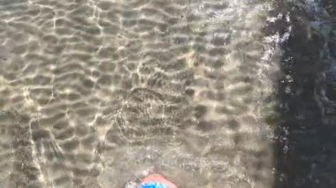 Çıplak ayaklı ıslak sahil kumu. Erkek bacakları ve ayakları kumlu sahilde deniz dalgaları boyunca yürüyor. Adam deniz kıyısında sörf yapıyor. Su ve köpük damlaları. yavaş çekim.