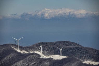 Güney Kore 'nin Gangwon Eyaleti Hoengseong İlçesi' ndeki Taegi Dağı 'nın karla kaplı zirvesinde bir rüzgar türbininin uzaktan görüntüsü..