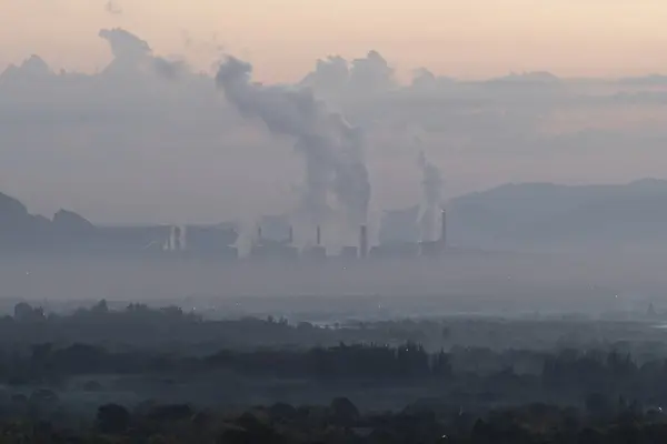 A factory emits smoke from its stacks, and Air pollution over the coal power plant Mae Moh Lampang in the morning with fog, Suitable for industrial and environmental themes
