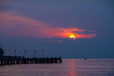 Ateşli turuncu güneş ufkun altına batar, gökyüzünü ve suyu boyarken nefes kesen yaz günbatımında