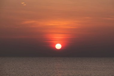Ateşli turuncu güneş ufkun altına batar, dalgalanan okyanus dalgaları üzerinde sıcak bir parıltı bırakır.