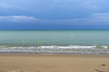 Pofuduk bulutlar, tropikal bir plajın üzerinde, kıyı şeridinde turkuaz dalgalar eşliğinde parlak bir yaz gökyüzünde sürükleniyor.