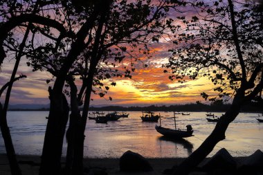 Huzurlu bir sükunet içinde, turuncu gökyüzünün gün batımında deniz suyunu yansıttığı güzel bir akşam manzarasında dinlenen orman teknesi.