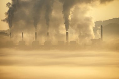 Dumanla kaplı Skyline, siyah duman püskürten endüstriyel bacalar, kalın bir sis örtüsüyle örtülmüş. Güneşin altın ışığı hava kirliliğiyle savaşıyor..
