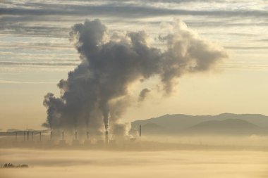 Endüstriyel Şafak, büyük bir enerji santrali endüstriyel kompleksinin görüntüsü, güneş doğarken altın gökyüzüne yükselen duman bulutları..