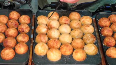 Bir şef, Japonya 'dan sevilen bir sokak yemeği olan altın, kıtır kıtır takoyaki toplarını pişiriyor ve çeviriyor.