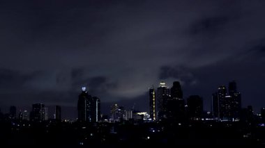 Karanlık yağmur bulutları Bangkok silueti boyunca ilerlerken gök gürültüsü gecenin içinde gürlerken.