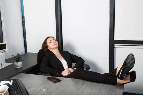 Beautiful business woman relaxing with her feet on the desk in office. Businesswoman sits worker close eyes sitting. Female boss worker sitting with legs on the table in the resting time at work place