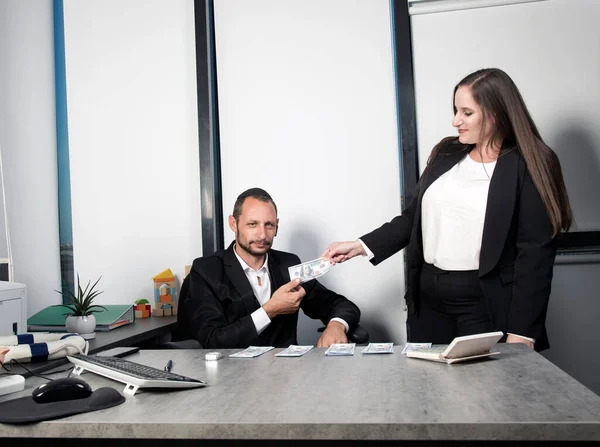 Jew receiving salary money. Serious jewish man in formal wear sit at desk wearing kippah bonus money from boss at office happily. Caucasian female with long hair is holding hundred dollar bill