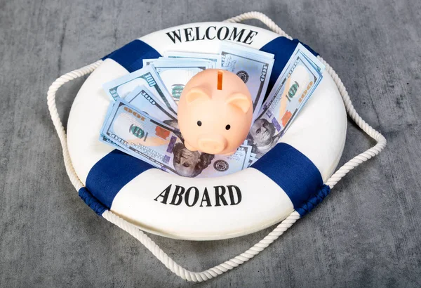 Blue and white life buoy on wooden desk background. Piggy bank on stacked dollars banknotes and lifebuoy with text Welcome on Board. Assets wealth, money saving and security by insurance concep