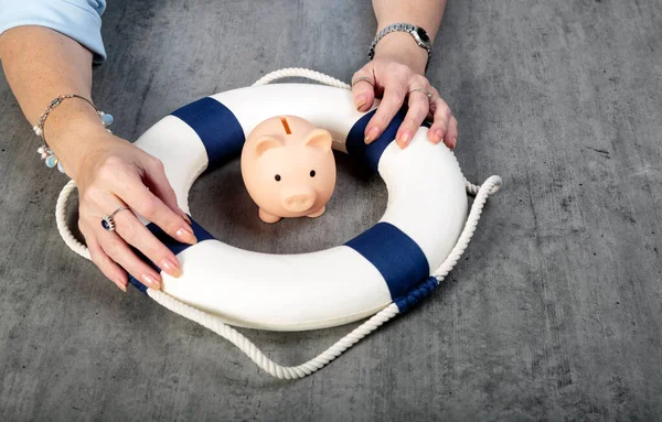 Woman hands with little piggy bank inside of lifebuoy, Safe Money. Blue and white life buoy on wooden desk table background. Assets wealth, money saving and security by insurance concept. Copy space.