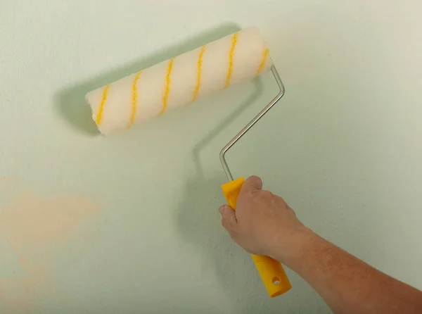 Woman using paint roller with a yellow handle. Building, renovation and construction work. Tools for painting walls. Human Hand holding new roller brush. A men hand hold paint roller and painting wall