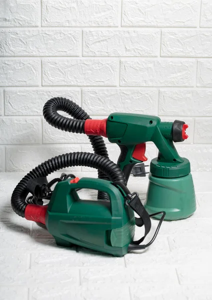 Electric green colored paint sprayer over a white brick background. Useful Instrument for quick paint jobs. New spray gun technology used by professionals, clean and efficient device for renovation