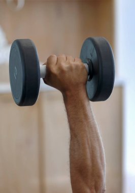 Bulanık bir arka planda, kasların dayanıklılığı üzerinde çalışan aptal bir adam. Kas yığını bir erkek eli, spor salonunda ağır bir dambılı kaldırıyor. Elinde dambıl tutan güçlü bir adamın kesilmiş fotoğrafı.