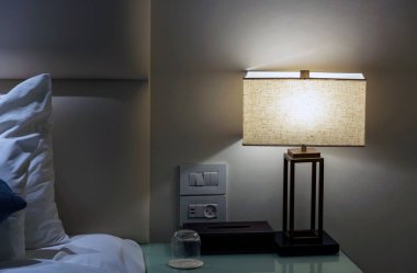 Yatağı, yastıkları ve beyaz pamuklu çarşafları olan çağdaş tarzda beyaz oda içiyle komodinli lamba. Yatak odasının iç kısımları. Modern stil komodindeki komodin lambası..