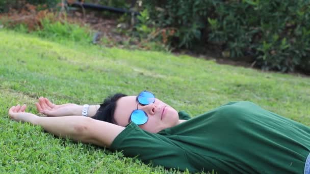 Дівчина Чорним Волоссям Сонцезахисних Окулярах Зелена Блузка Лежить Траві Парку — стокове відео