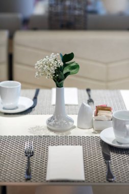 Masanın ortasına beyaz çiçekli bir vazo yerleştirilir, yemek takımları, fincan tabakları ve çatal bıçaklar da dahil olmak üzere. Küçük bir şeker kabı.