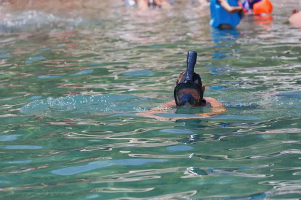 A person snorkeling in clear greenish water. Only the top of the man head along with a black snorkel full face mask diving are visible above the water. Underwater swimming in Red sea. Water sport