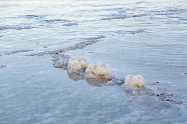 Sığ sulardan çıkan kristalize oluşumlara sahip tuz düzlüğü. Beyaz tuz kristalleri mavi suyun yumuşak renkleriyle tezat oluşturur. İsrail 'de Ölü Deniz' in tuz mineral doğal oluşumunu kapatın.