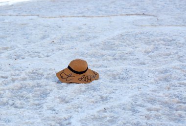 Geniş, dekore edilmiş ve siyah tasarımlı hasır şapka, açık yaz güneşinin altında, Ölü Deniz 'in beyaz kristal yüzey tuzlu plajında yatıyor. İsrail, sahil şeridinde tuz oluşumları