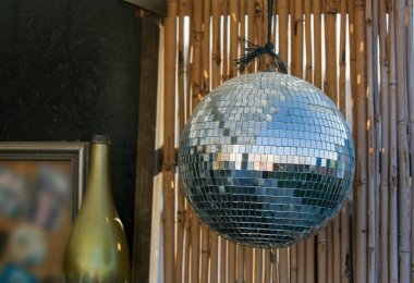 Bambu arka planının önünde asılı disko topunun görüntüsü ışığı yansıtır ve canlı bir atmosfer yaratır. Disko, parti, müzik, dans, eğlence ve gece kulübü konsepti. Kristal disko ayna küresini kapat
