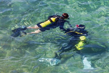 İki dalgıcın denizin yüzeyinde yüzdüğü görüldü. Siyah dalış kıyafeti giyiyorlar ve sarı oksijen tankları var. Şnorkel ve maskeyle donatılmış halde sualtı keşfi için hazırlar.