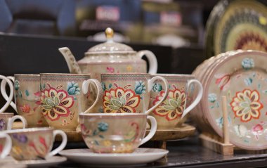 Karmaşık çiçek desenli koyu arkaplanlı porselen bir çay seti. Set fincanlar, çay tabakları, çaydanlık ve tabakları içeriyor. Her parça canlı çiçek ve yapraklarla süslenmiş..