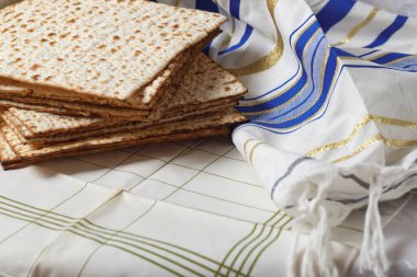 Bir yığın matzo, mayasız ekmek, bir Tallit 'in yanında, bir Yahudi dua şalı. Matzo ve Tallit beyaz ve yeşil desenli kumaşla kaplı bir yüzey üzerindeler. Yahudi Hamursuz Bayramı.