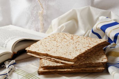 Bir yığın matza, bir kitap ve bir tallit. Matzo ön planda. Onun yanında açık bir kitap var Tora. Mekan huzurlu ve dindar görünüyor. Geleneksel Yahudi bayramı.