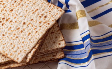 Yahudi bayramı. Bir yığın matzo, mayasız ekmek, bir Tallit 'in yanında, bir Yahudi dua şalı. Matzo ve Tallit beyaz ve yeşil desenli kumaşla kaplı bir yüzey üzerindeler..