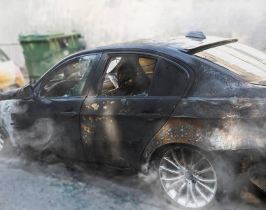 Yanmış bir araba, yanmış kalıntılardan yükselen dumanla bir şehir caddesinde duruyor. Yanmış bir araç duvara dayanıyor, duman yayıyor, camlar kırılıyor, kentsel ortam, İsrail ve Hayfa 'da hasar görüyor.