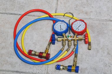 Gauges have measurement scales, are used for diagnosing air conditioning systems. Set of HVAC manifold gauges with three hoses in blue, yellow and red colors, connected to corresponding colored valves clipart