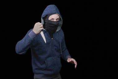 Koyu renk kapüşonlu bir adam loş bir ortamda dikilip bıçakla saldırıyor. Karanlıkta kanlı bıçaklı kapüşonlu adam. Erkek yüzü maske tarafından gizleniyor, bu da anonimliği arttırıyor.