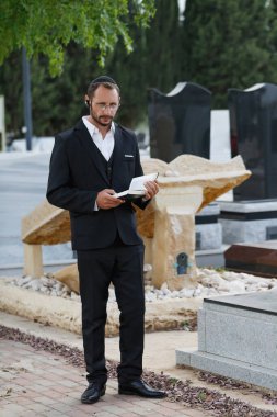 Resmi siyah takım elbiseli Yahudi erkek mezar taşlarıyla çevrili bir mezarlıkta duruyor. Sakallı Yahudi bir adam, kippah takıyor, Tevrat 'tan bir dua okuyor. Merhum için dua, cenaze.