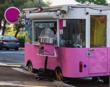 Parlak pembe bir dondurma arabası, yeşil ağaçların gölgesinin altında, sessiz bir caddede, eğlenceli tasarımlarla park edilmiş. Sahne kaygısız ve davetkar bir yaz öğleden sonrasını yakalıyor, harika bir atıştırmalık için.