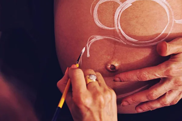女画家画孕妇的腹部与身体油漆和刷子 — 图库照片