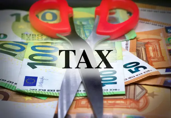 Scissors cutting word tax with banknotes as background. Business, finance and profit concept.