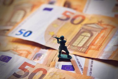 Toy soldier on Euro bills banknotes, war costs concept. clipart