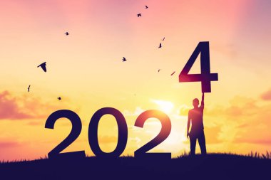 İnsanlar günbatımı gökyüzünde dağın tepesinde uçan kuşlar ve 2024 gibi soyut bir sayı ile el kaldırır. Mutlu yıllar ve tatil konsepti. Klasik ton filtre efekti renk biçimi.