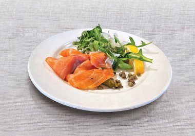 Taze somon dilimleri, roka salatası, limon, salatalık turşusu ve kapari ile servis edilir.