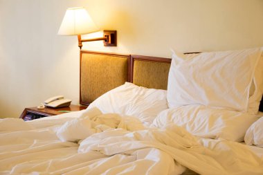 Dağınık beyaz yatak, yastık ve lamba.