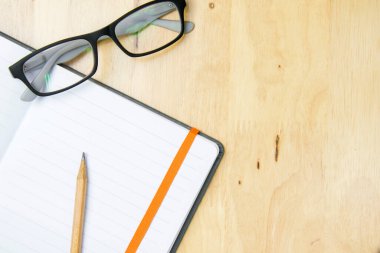 Çalışma alanı tahtasına defter konmuş gözlük ve kahverengi kalem. Üst görünüm, düz görünüm kavramı.