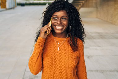 Gülümseyen Afrikalı Amerikalı kadın sokakta yürürken telefonda konuşuyor. Teknoloji konsepti.