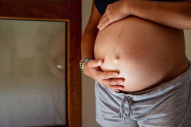 Evdeyken karnına dokunan hamile bir kadının yakın görüntüsü. Annelik kavramı.