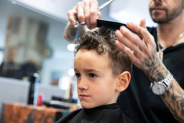 Hairdresser combing and cutting a boys hair in his barbershop. Hairdressing and childhood concept.