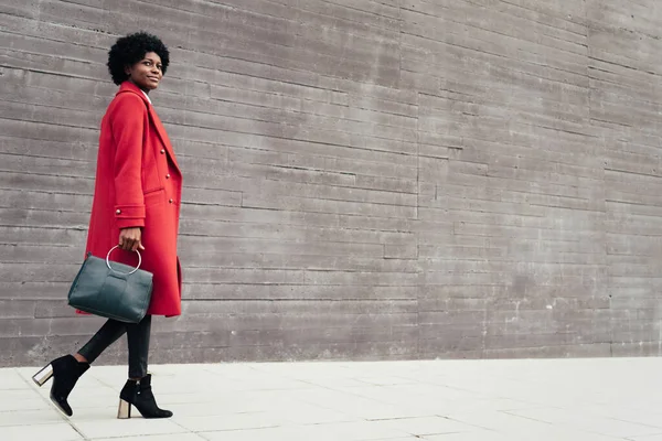 Stilvolle Afro Frau Mit Handtasche Und Rotem Mantel Während Sie lizenzfreie Stockfotos