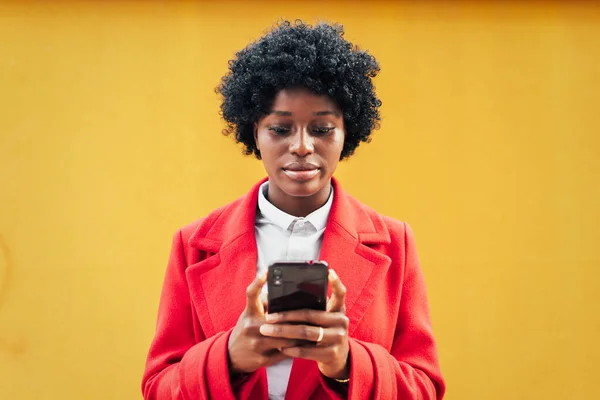 Afro Kobieta Pomocą Telefonu Komórkowego Stojąc Pod Żółtą Ścianą Koncepcja Zdjęcie Stockowe
