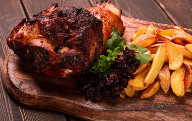 Pork knuckle, in soy-honey sauce, with fried potatoes, on a wooden chopping board, homemade, no people,