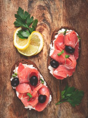 Krem peynirli sandviçler, somon balığı, soğuk tütsülenmiş tahıllı ekmek, kesme tahtasının üstünde, üst manzara, kahvaltı, limon ve maydanoz, insan yok.,