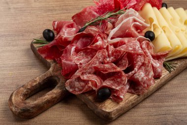 Çeşit çeşit et, aperatif, prosciutto, salam ve jambon, maasdam peyniri ve zeytinlerle ahşap bir tahtada, kahvaltı, üst manzara, yakın çekim, insan yok.